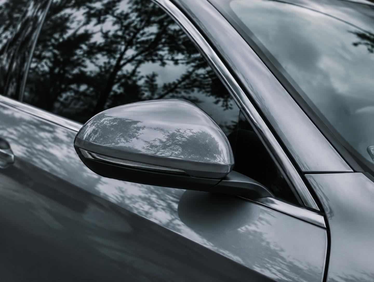 A silver side mirror and window with trees and clouds reflected cleanly in the glass and paint.