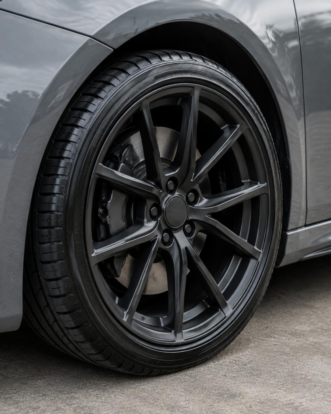 A clean dark multi-spoke alloy wheel and freshly dressed tyre on a grey car.